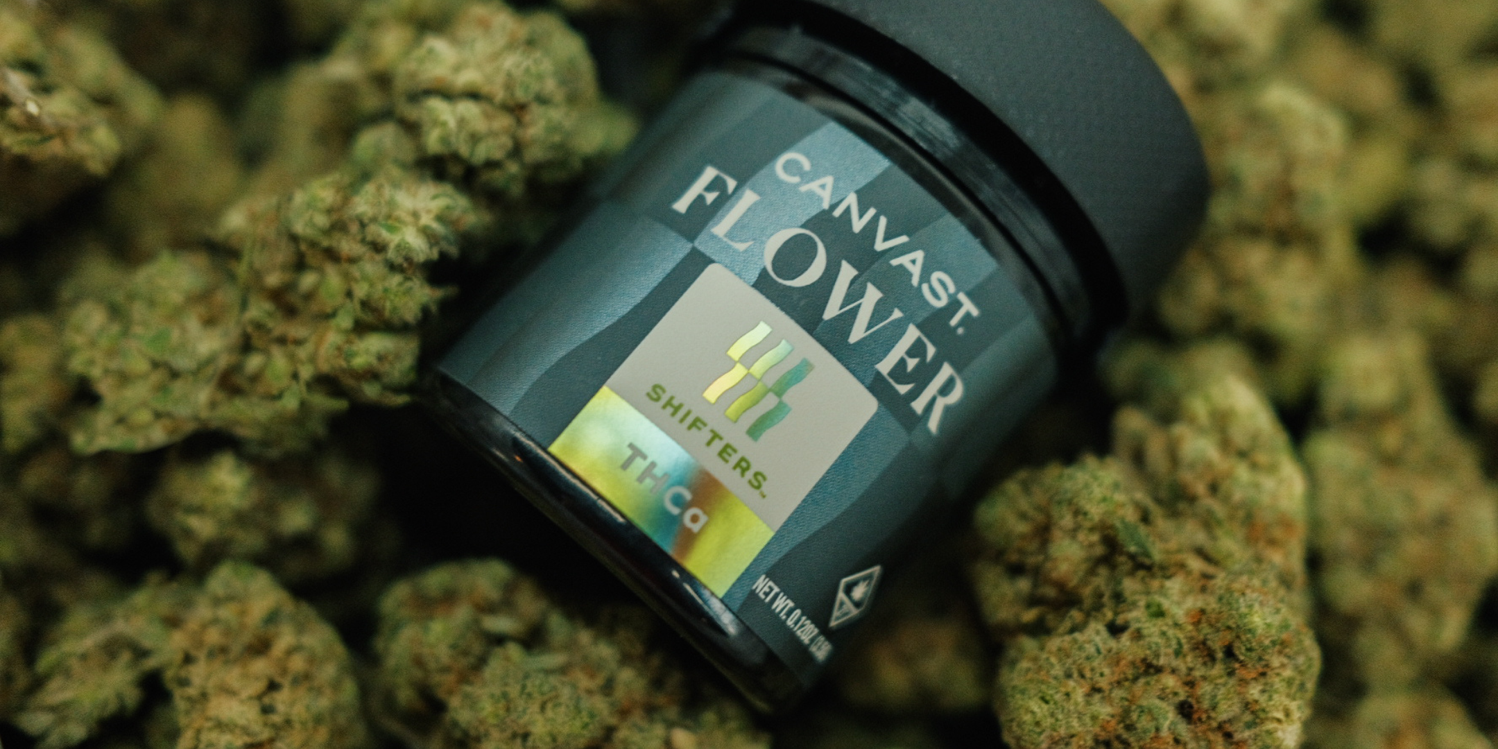 A jar of Canvast THCa Hemp Flower laying on top of loose flower buds