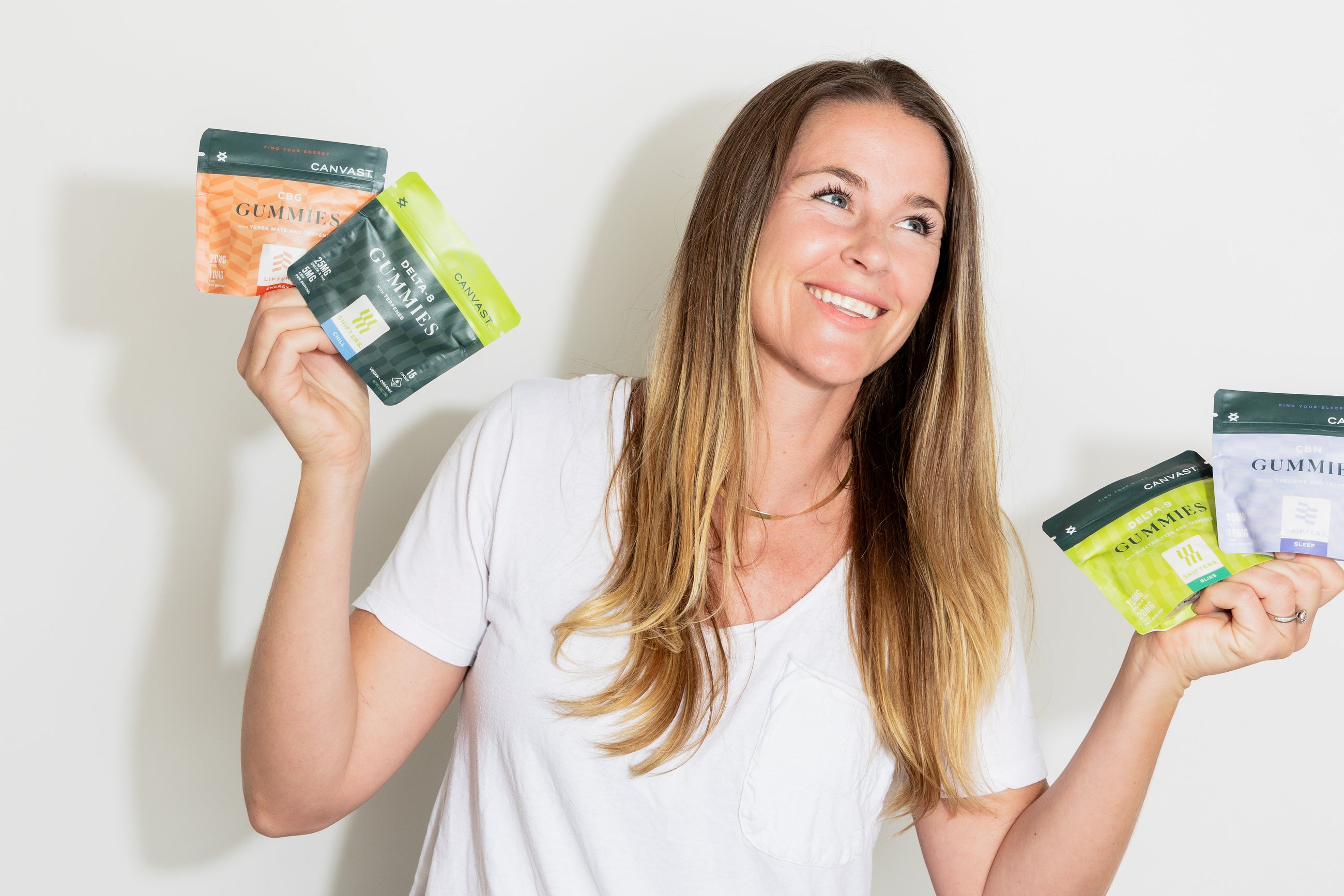 Woman smiling and holding 2 bags in each hand of Canvast Gummies