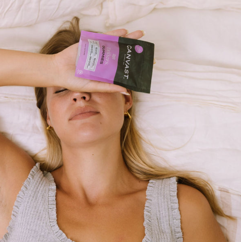 How Does CBD Help with Anxiety Disorders? Woman relaxing in bed with CBD, CBN gummies to help with sleep and anxiety relief.