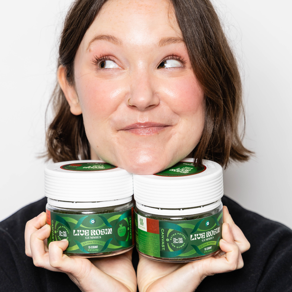 Woman holding 2 jars of sour apple live rosin gummies on a white background