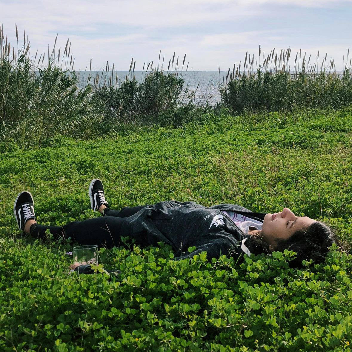 Woman laying in green grass under a bright blue sky, relaxing outdoors in a peaceful, natural setting—representing calm, balance, and the body’s endocannabinoid system working in harmony with cannabis.