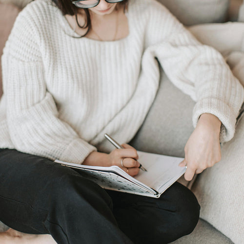 Woman sitting on couch writing in her journal - Setting goals in the new year.