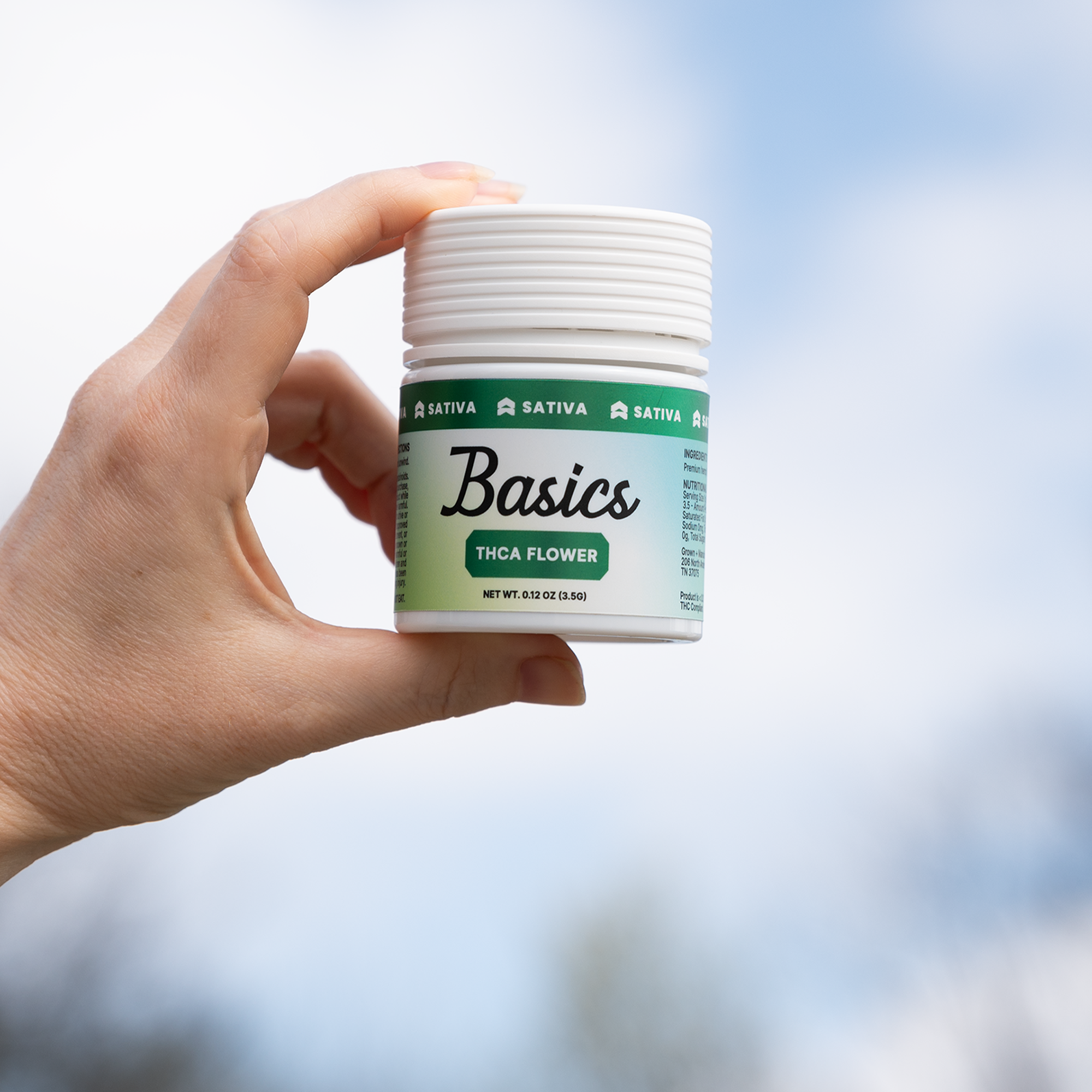 Hand holding THCa flower with a green and blue label with a blue sky background. Basics Premium Hemp Flower.