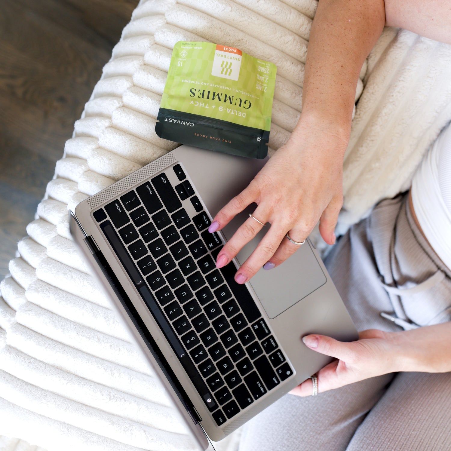 A person working on a laptop on a bed next to a bag of Shifters™ Focus Gummies with THCv + Delta-9 THC and terpenes.