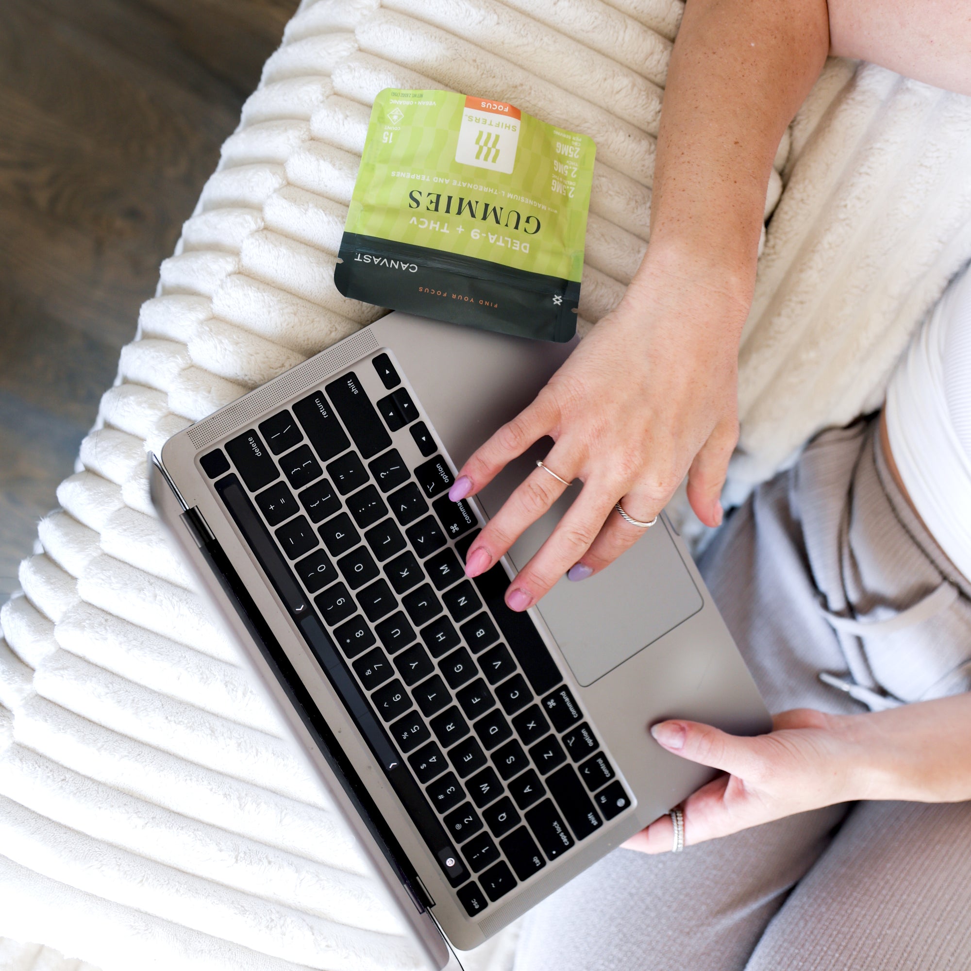 A person working on a laptop on a bed next to a bag of Shifters™ Focus Gummies with THCv + Delta-9 THC and terpenes.