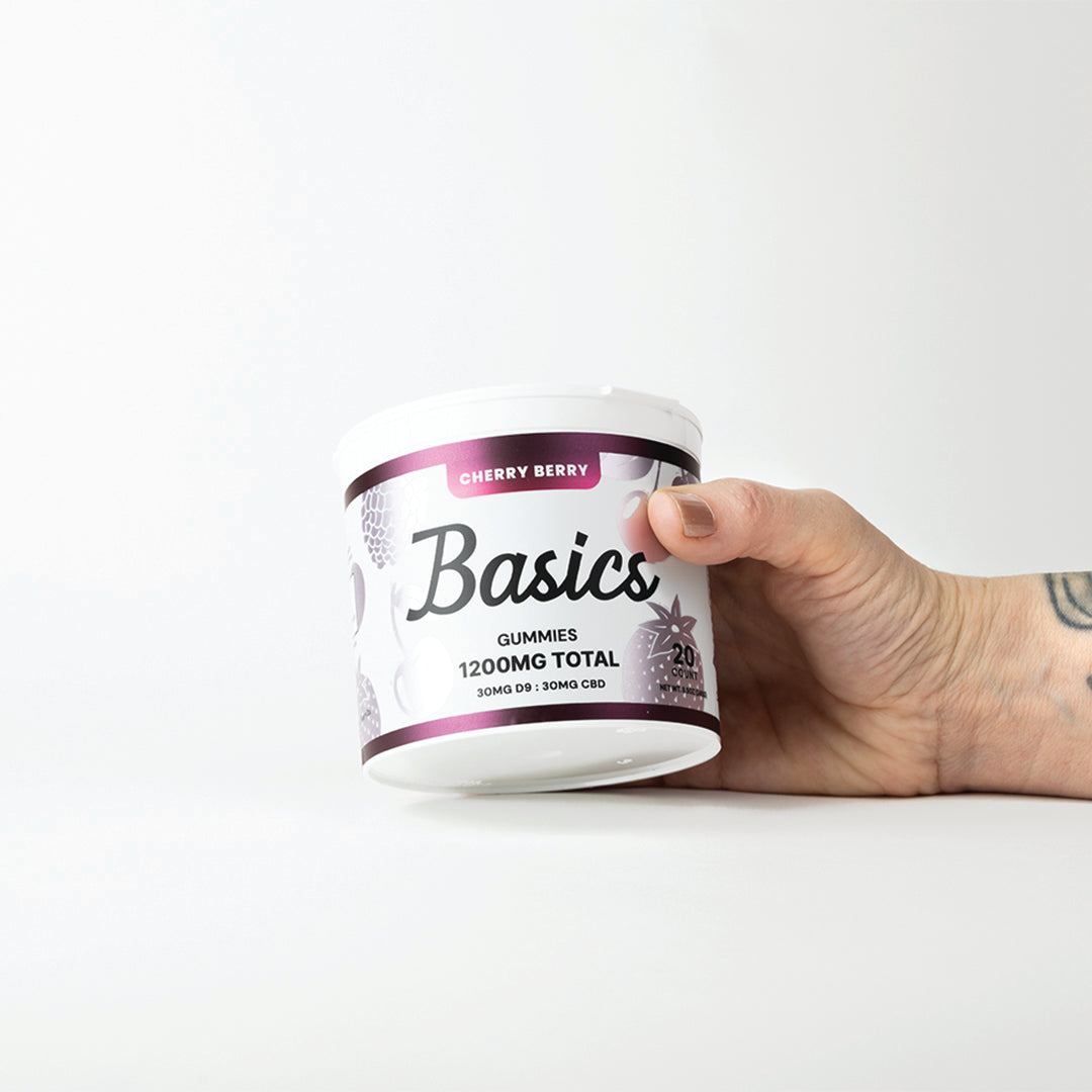 Hand holding a container labeled 'Basics' with purple and white design on a white background. 1200mg total cannabinoids. 30mg Nano D9 THC + 30mg CBD.