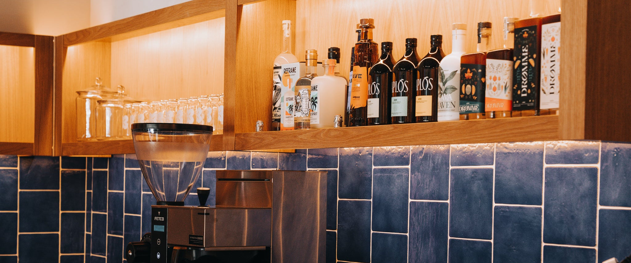 Bar area with blue tiled wall, wooden shelves, and various bottles.