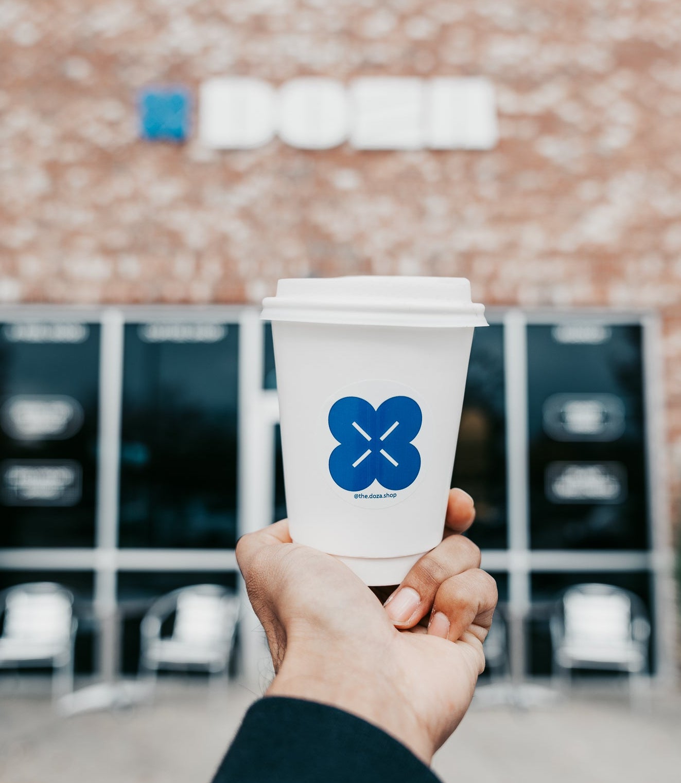 Hand holding a coffee cup with a blue logo in front of a building
