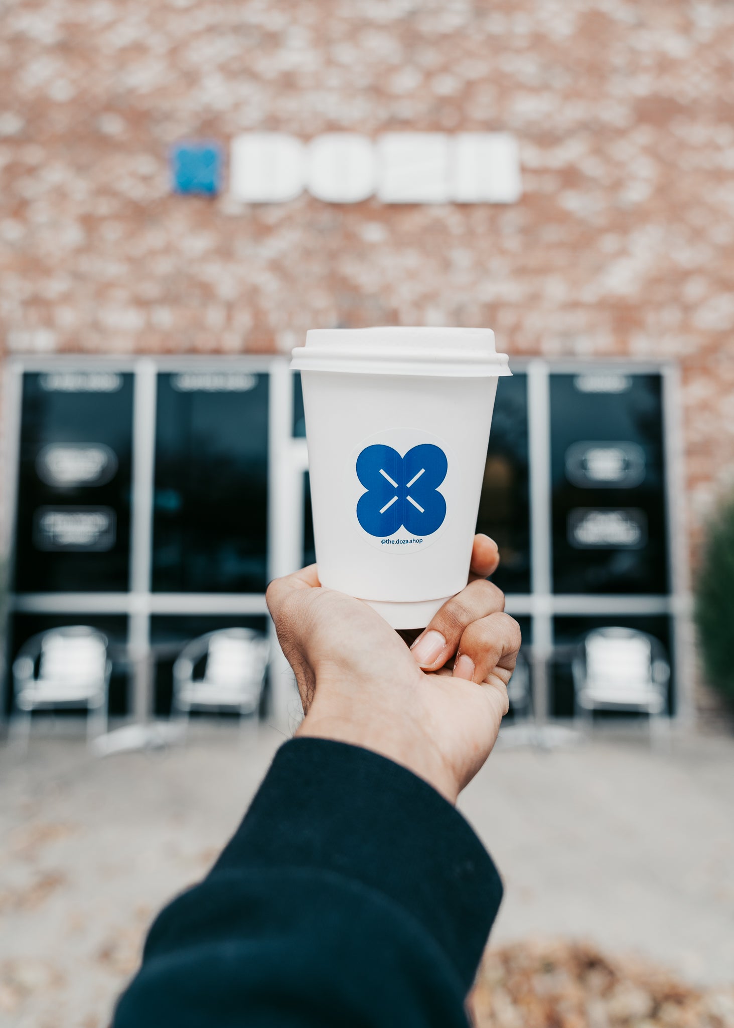Hand holding a coffee cup with a blue logo in front of a building - Doza Coffee and Wellness in Hendersonville, TN